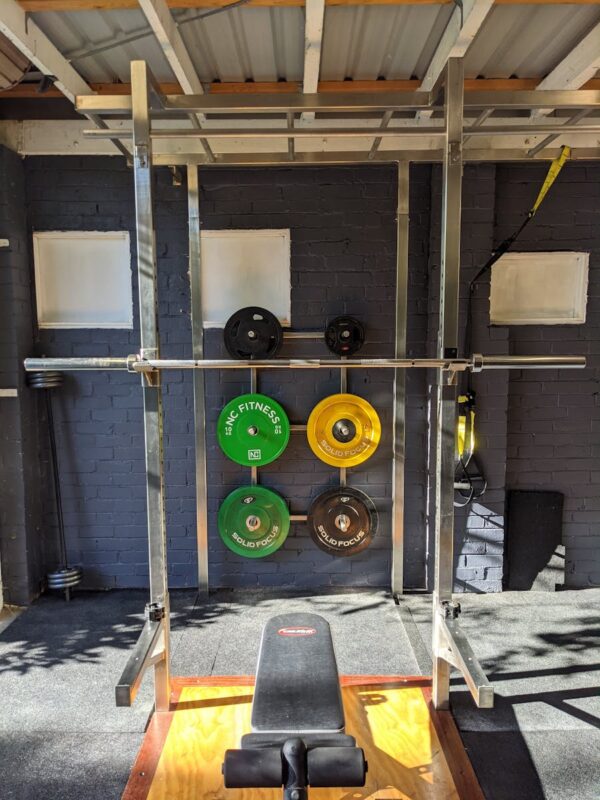 A well-equipped home gym featuring a squat rack, weights, and a bench.