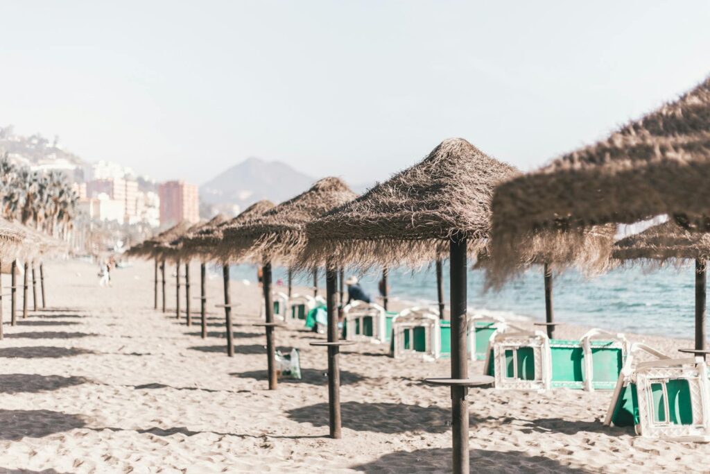 A serene sandy beach with straw umbrellas and clear skies, perfect for a summer vacation in Malaga, Spain.