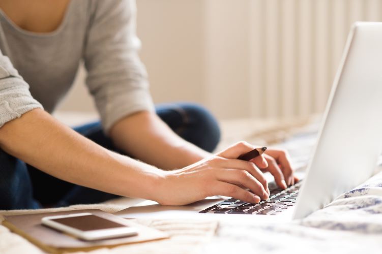 graphicstock-unrecognizable-young-woman-sitting-on-bed-working-on-laptop-smart-phone-next-to-her-home-office_SumRk2SGb