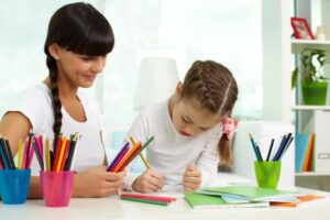 Portrait of cute girl drawing with colorful pencils with her mother near by