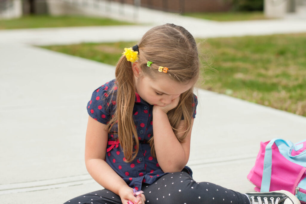 Caucasian,Sad,Little,Girl,Sitting,On,A,Sidewalk,In,Front