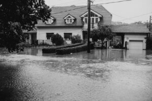 A black and white image showing a suburban house surrounded by floodwater.