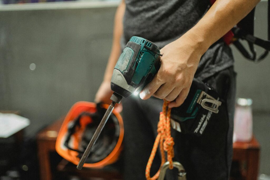 A worker holding a power drill and helmet, ready for maintenance tasks.