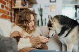 Woman relaxing on couch with a Siberian Husky, creating a cozy and warm atmosphere.