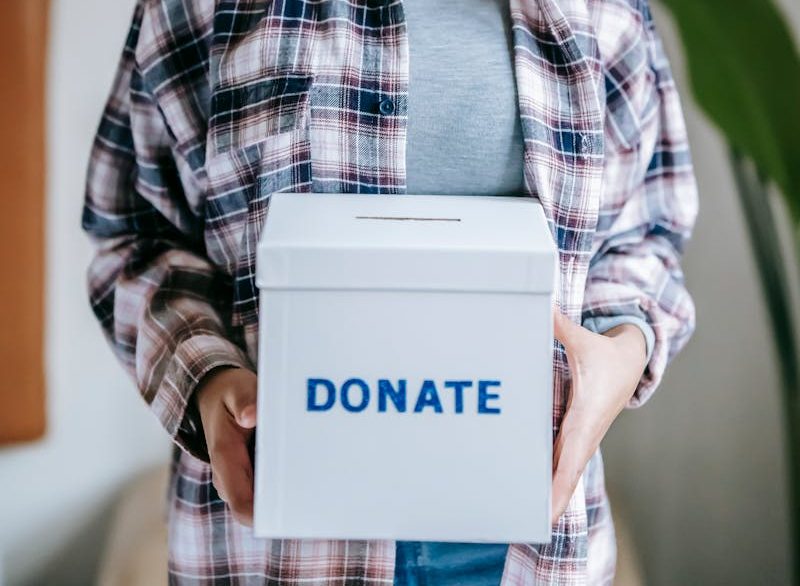 Cheerful woman holding a box labeled 'Donate' indoors, symbolizing charity and kindness.