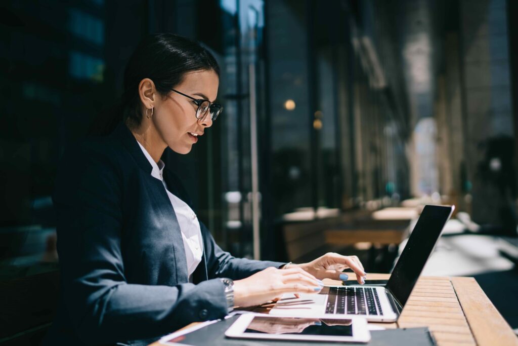 Side view of serious female economist working online with accounting documents on modern laptop device during sunny day in street cafeteria, caucasian businesswoman typing name for media files