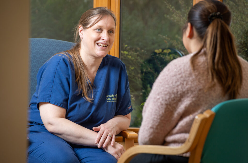 A City Hospice member, wearing a blue uniform, chatting to a patient.