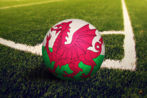 Wales flag on ball at corner kick position, soccer field background. National football theme on green grass.