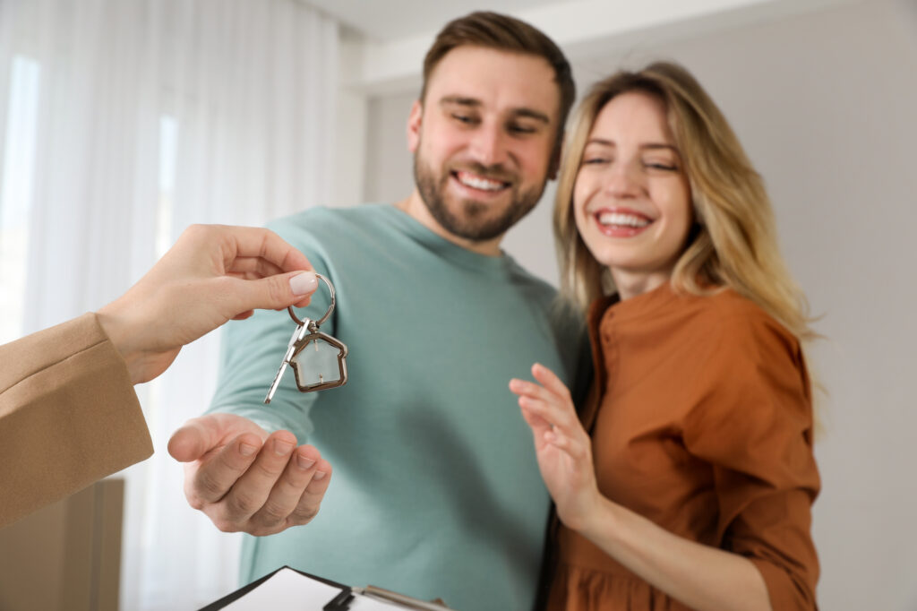 Real estate agent giving key to happy young couple in new house,