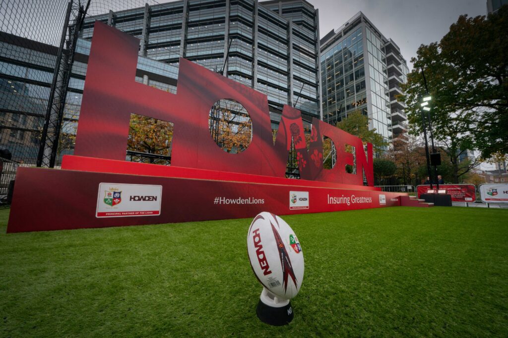 A branded Howden rugby ball on a green grass lawn in front of a large red Howden logo.