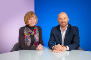 Anne Smith and Simon Tee sat at a white table against a purple and blue background.