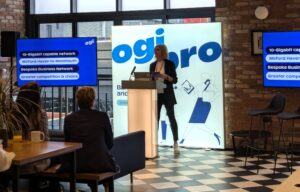 A person presenting at an event with the Ogi Pro logo in the background.