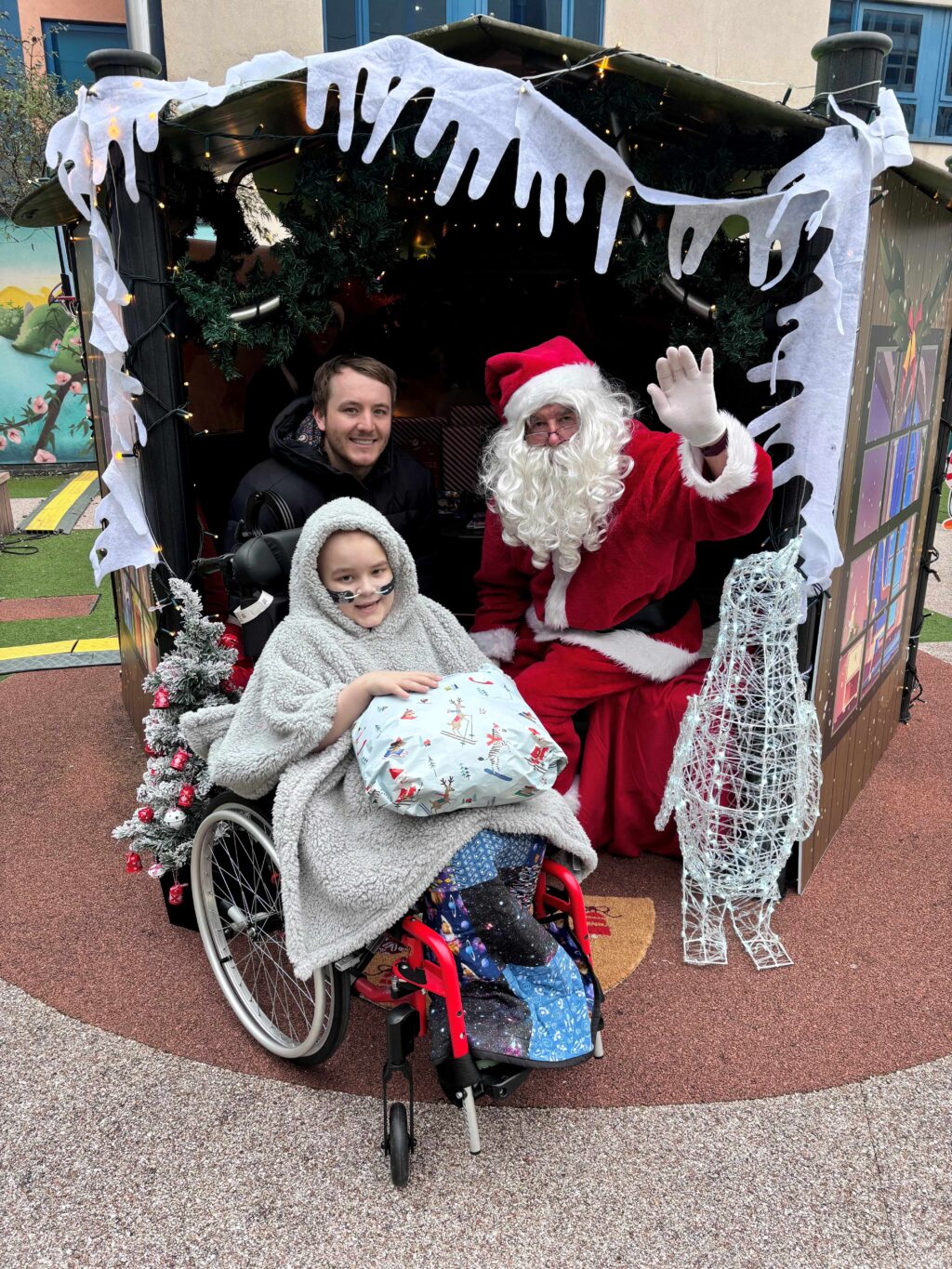 A young patient in a wheelchair in Santa's grotto with Santa.