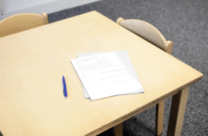 A white exam paper and black pen on a beige desk.