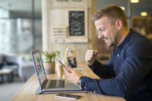 Happy freelancer with tablet and laptop computer in coffee shop.